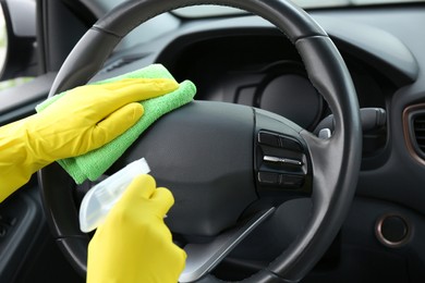 Photo of Woman cleaning steering wheel with rag in car, closeup