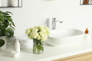 Photo of Beautiful roses and bath accessories near sink in bathroom