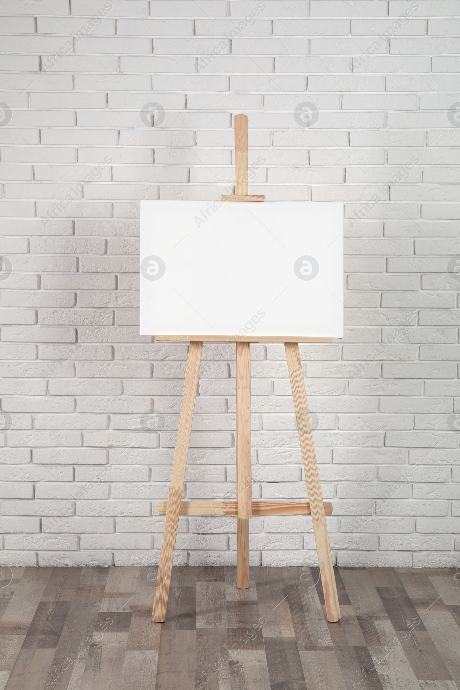 Photo of Wooden easel with blank canvas near white brick wall