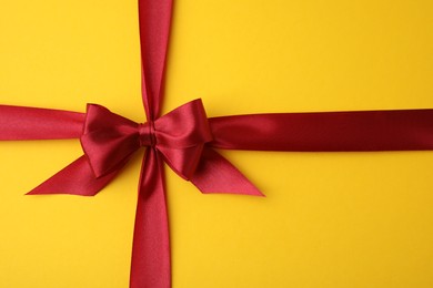 Photo of Red satin ribbon with bow on yellow background, top view