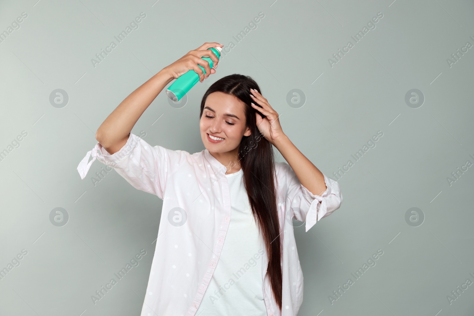 Photo of Woman applying dry shampoo onto her hair on light grey background