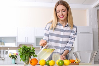 Photo of Young woman pouring lemonade into mason jar on table in kitchen. Natural detox drink