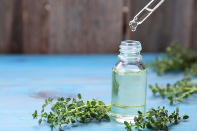 Photo of Thyme essential oil dripping from pipette into bottle on light blue wooden table, space for text