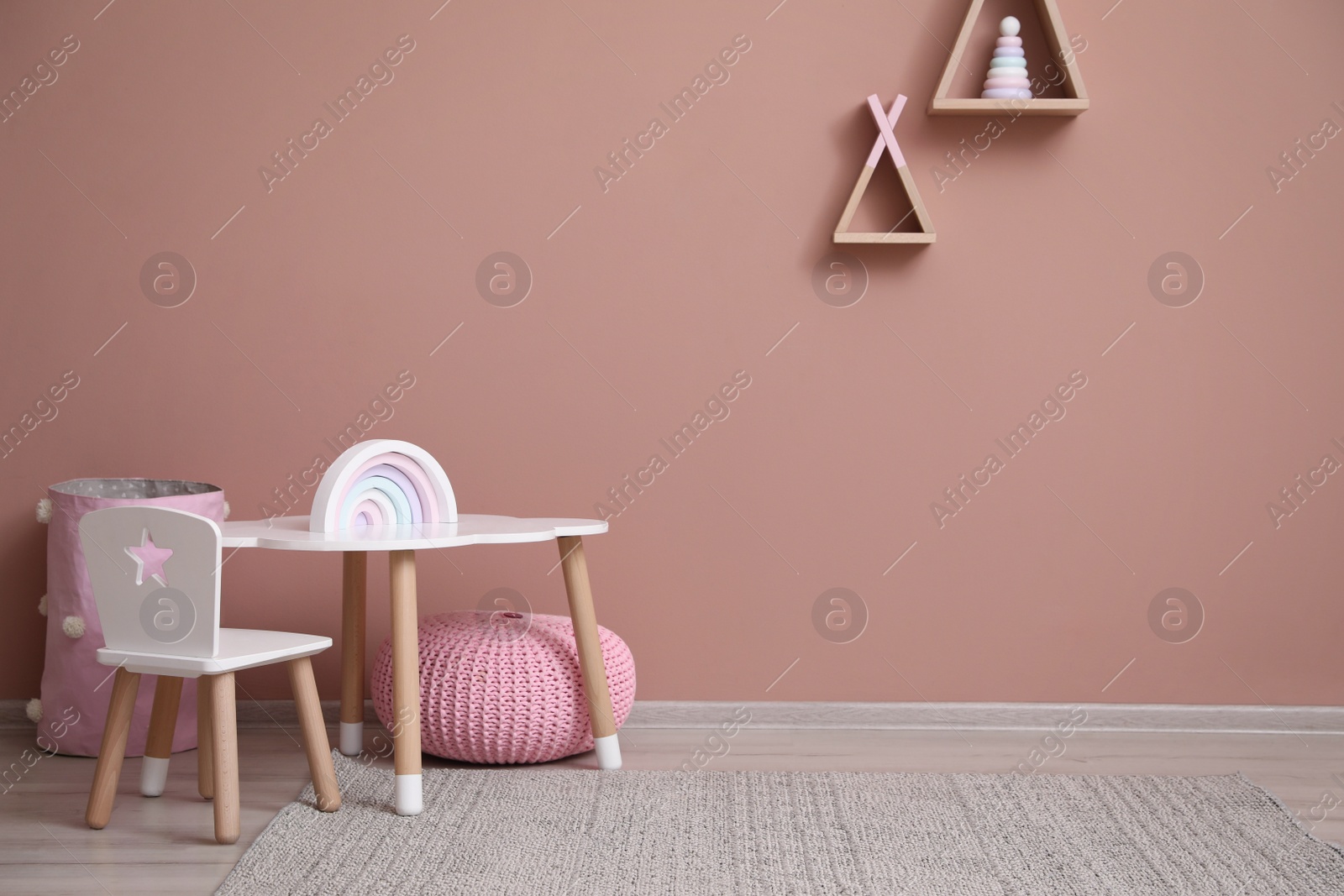 Photo of Cute child room interior with furniture, toys and wigwam shaped shelves on pink wall