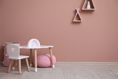 Photo of Cute child room interior with furniture, toys and wigwam shaped shelves on pink wall