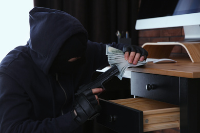 Dangerous masked criminal with gun stealing money from house