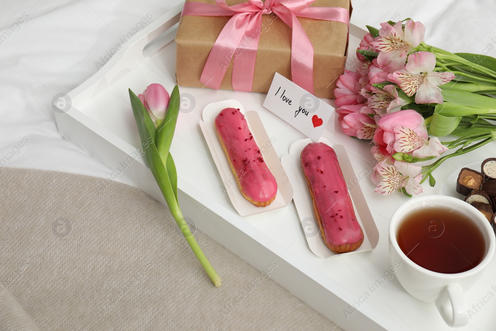 Photo of Tasty breakfast served in bed. Delicious desserts, tea, flowers, gift box and card with phrase I Love You on tray