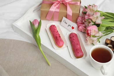 Photo of Tasty breakfast served in bed. Delicious desserts, tea, flowers, gift box and card with phrase I Love You on tray