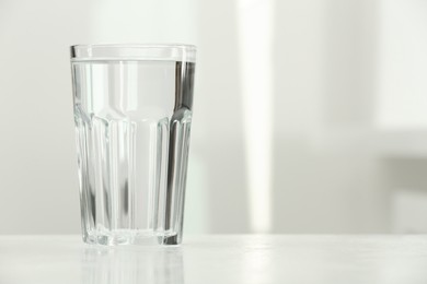 Glass of water on white table against blurred background, closeup. Space for text