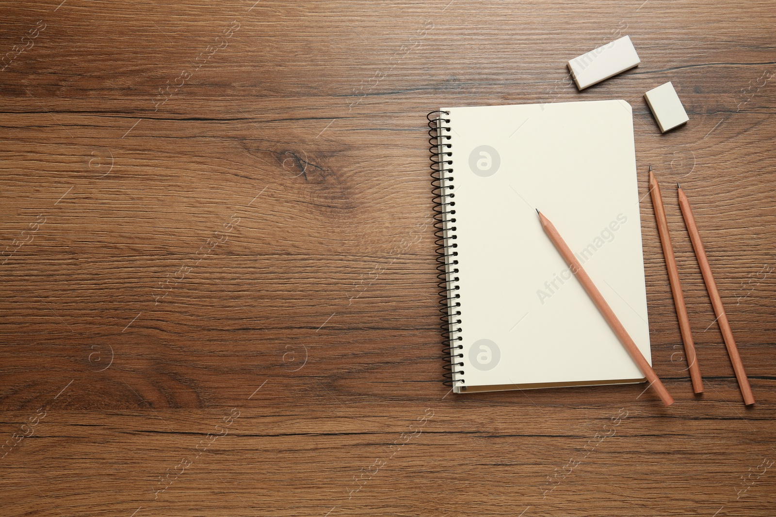 Photo of Sketchbook, pencils and erasers on wooden table, flat lay. Space for text