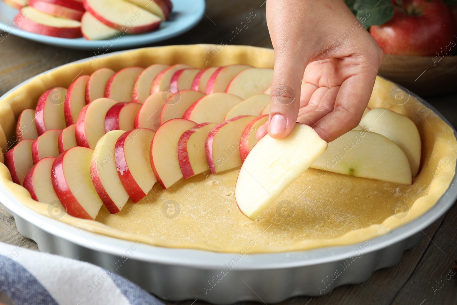 Photo of Woman putting apple slices into dish with raw dough at wooden table, closeup. Baking pie