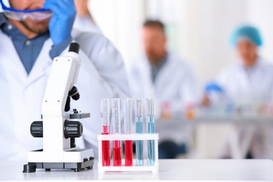 Photo of Rack with test tubes and microscope on table in laboratory, space for text. Research and analysis