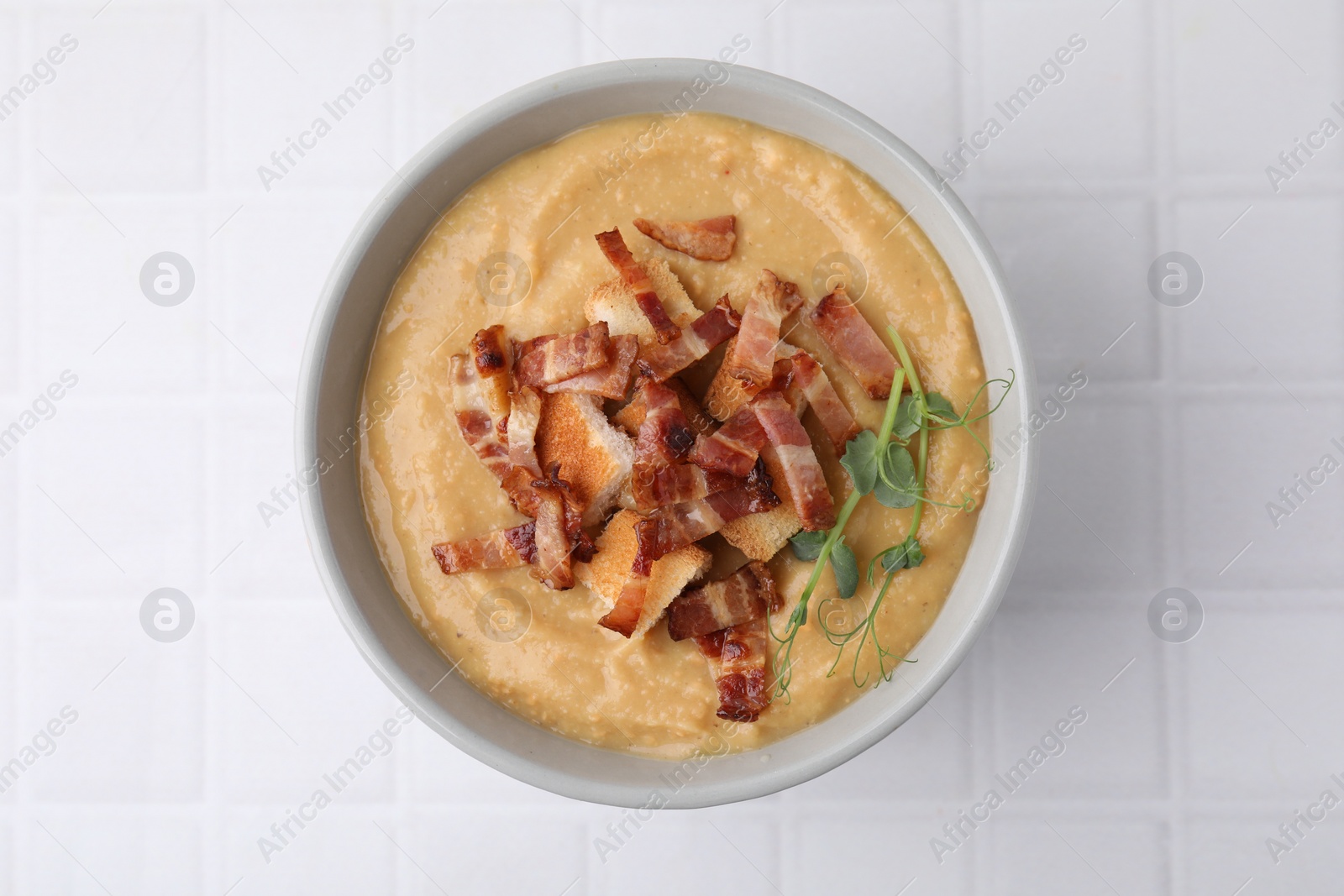 Photo of Delicious lentil soup with bacon and croutons on white tiled table, top view