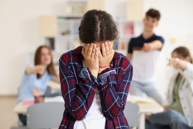 Teen problems. Students pointing at upset girl in classroom, selective focus