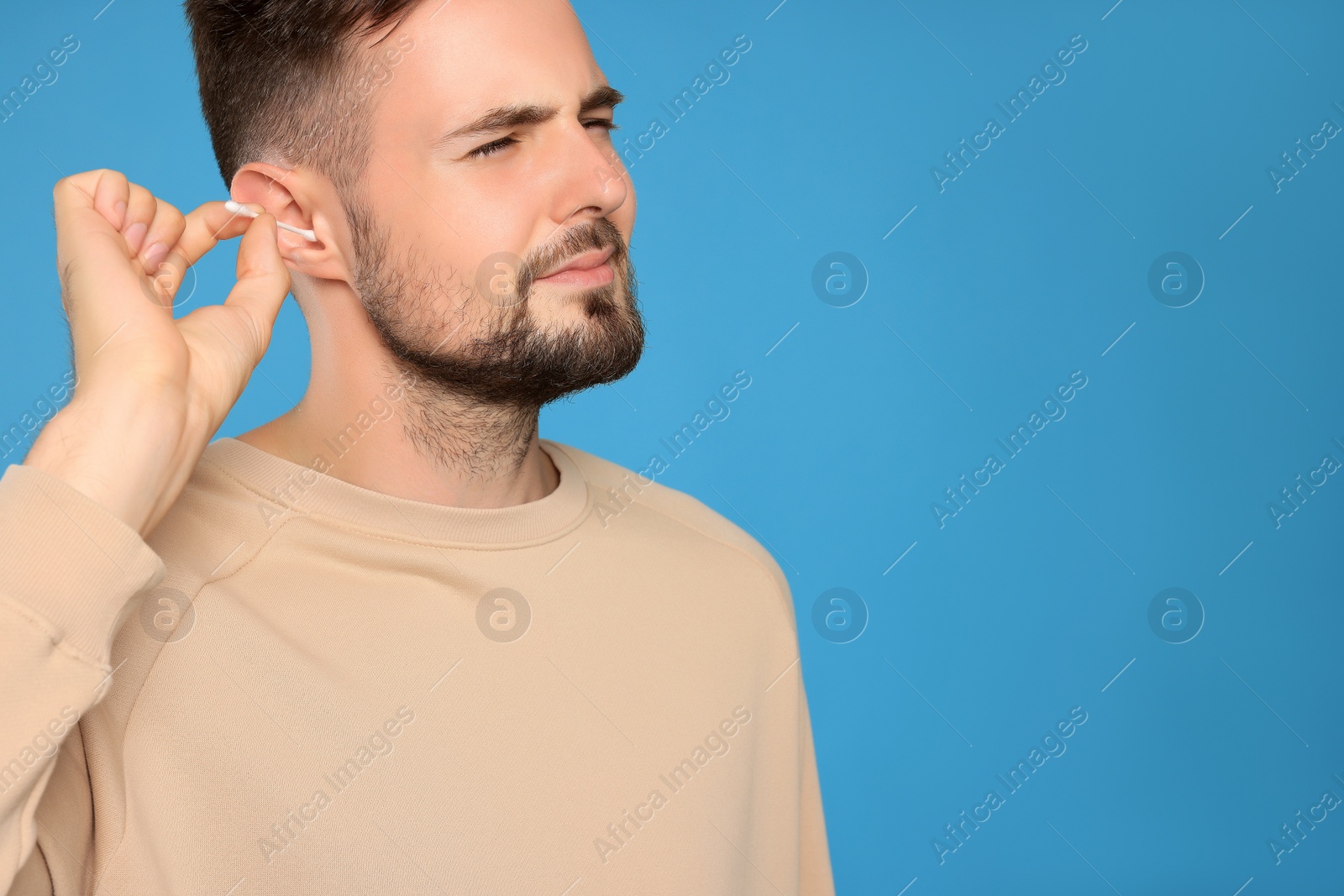 Photo of Young man cleaning ear with cotton swab on light blue background. Space for text