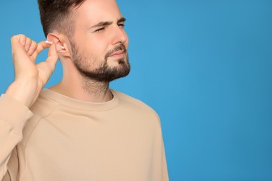 Young man cleaning ear with cotton swab on light blue background. Space for text