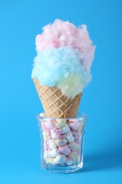 Photo of Sweet cotton candy in waffle cone on light blue background, closeup