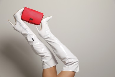 Photo of Woman wearing white long shoes with red leather bag on light background, closeup