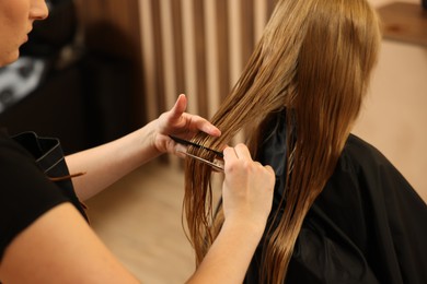 Photo of Professional hairdresser combing girl's hair in beauty salon, closeup