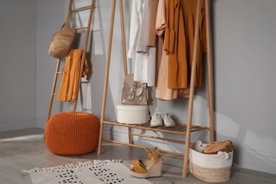 Modern dressing room interior with stylish clothes, shoes and orange pouf