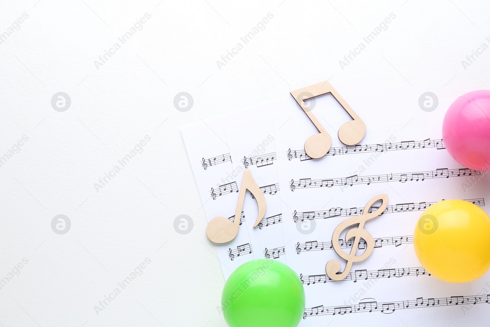 Photo of Wooden notes, music sheets and toy balls on white background, top view with space for text. Baby song concept