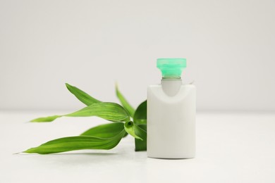 Photo of Mini bottle of cosmetic product and green branch on light background