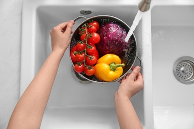 Photo of Woman washing fresh vegetables in kitchen sink, top view