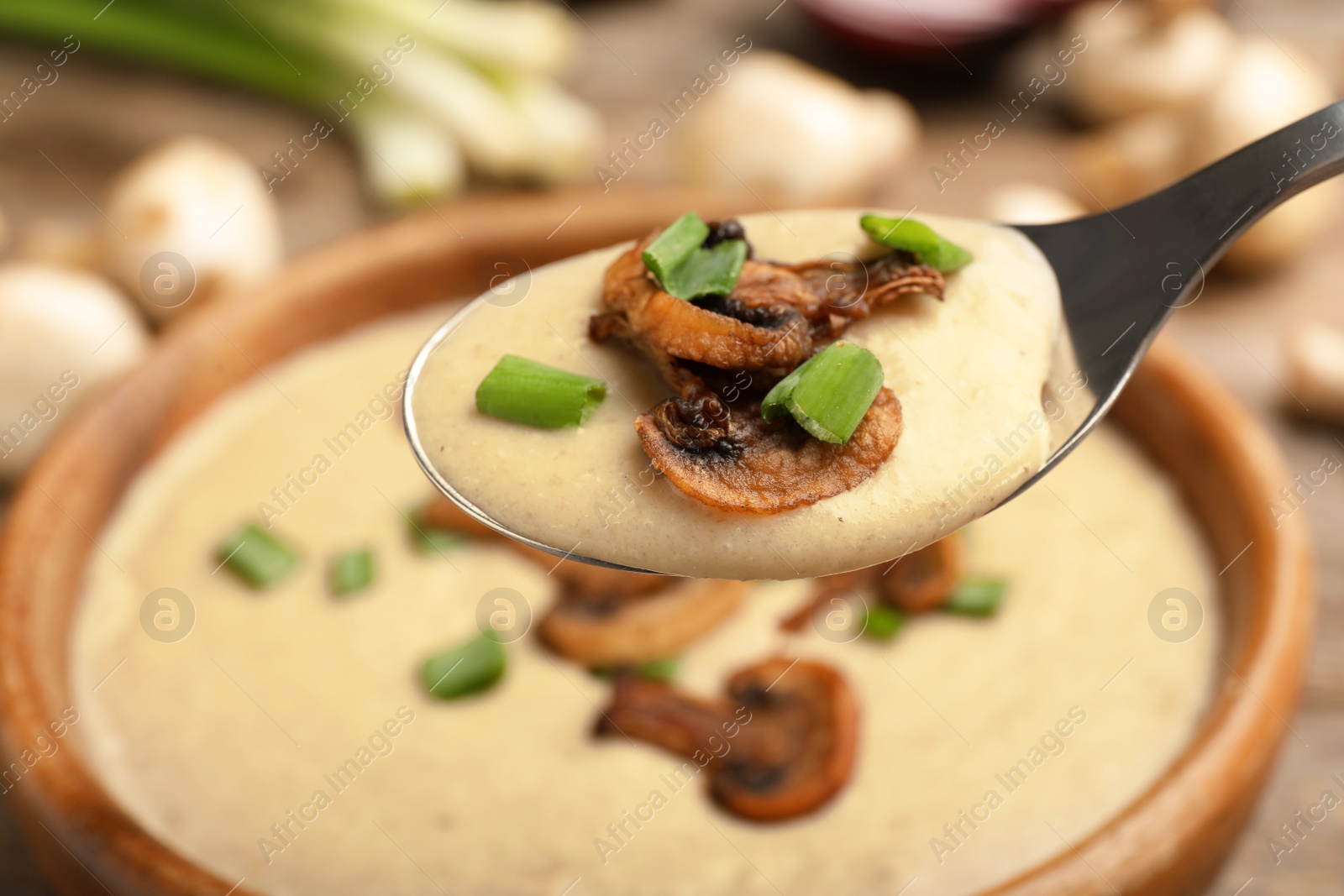 Photo of Spoon with fresh homemade mushroom soup over bowl, closeup