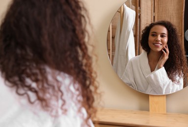 Beautiful African American woman in bathrobe near mirror at home