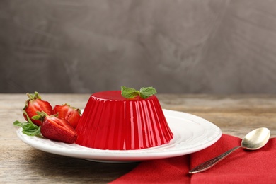 Photo of Plate of tasty strawberry jelly served on wooden table, space for text