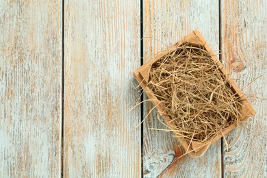 Photo of Dried hay in crate on light wooden background, top view. Space for text