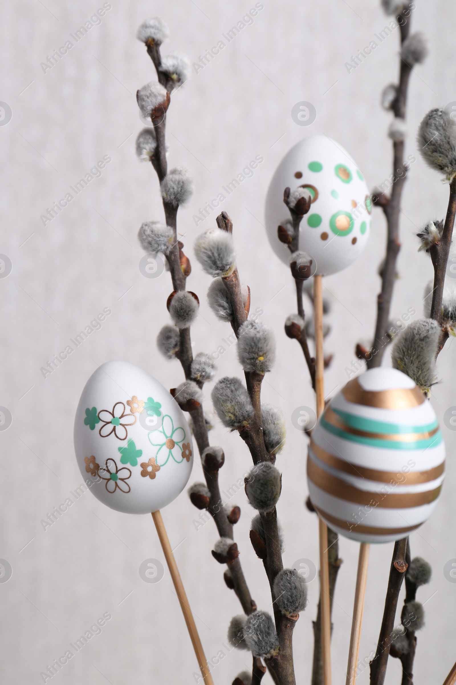 Photo of Beautiful willow branches with painted eggs on light grey background, closeup. Easter decor