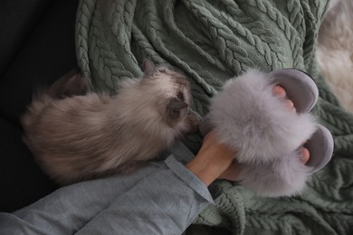 Photo of Woman in stylish soft slippers resting with cute cat at home, top view