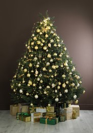 Photo of Beautifully decorated Christmas tree and many gift boxes near brown wall indoors