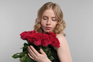 Photo of Beautiful woman with blonde hair holding bouquet of red roses on light grey background