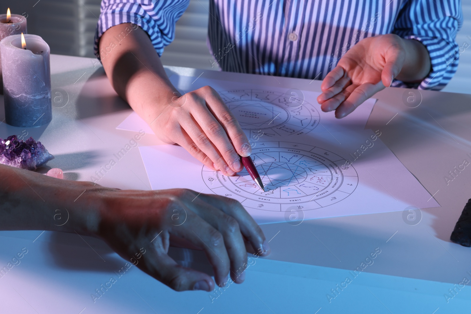 Photo of Astrologer showing natal charts to client at table indoors, closeup