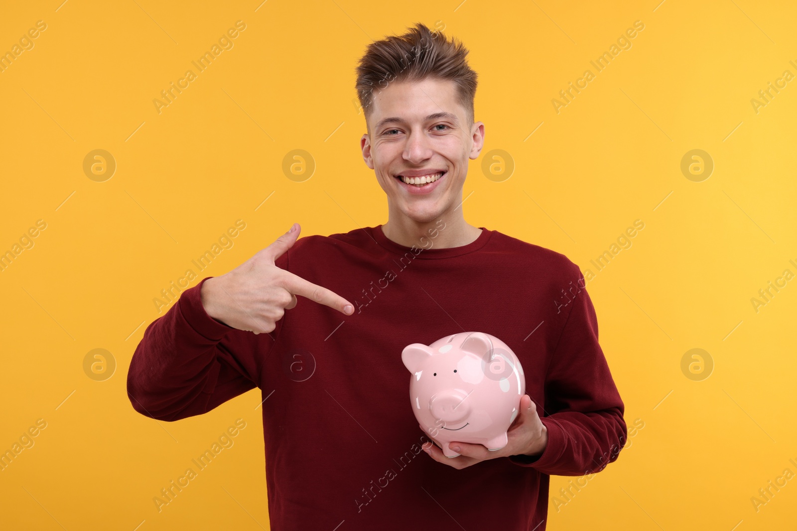 Photo of Happy man pointing at piggy bank on yellow background