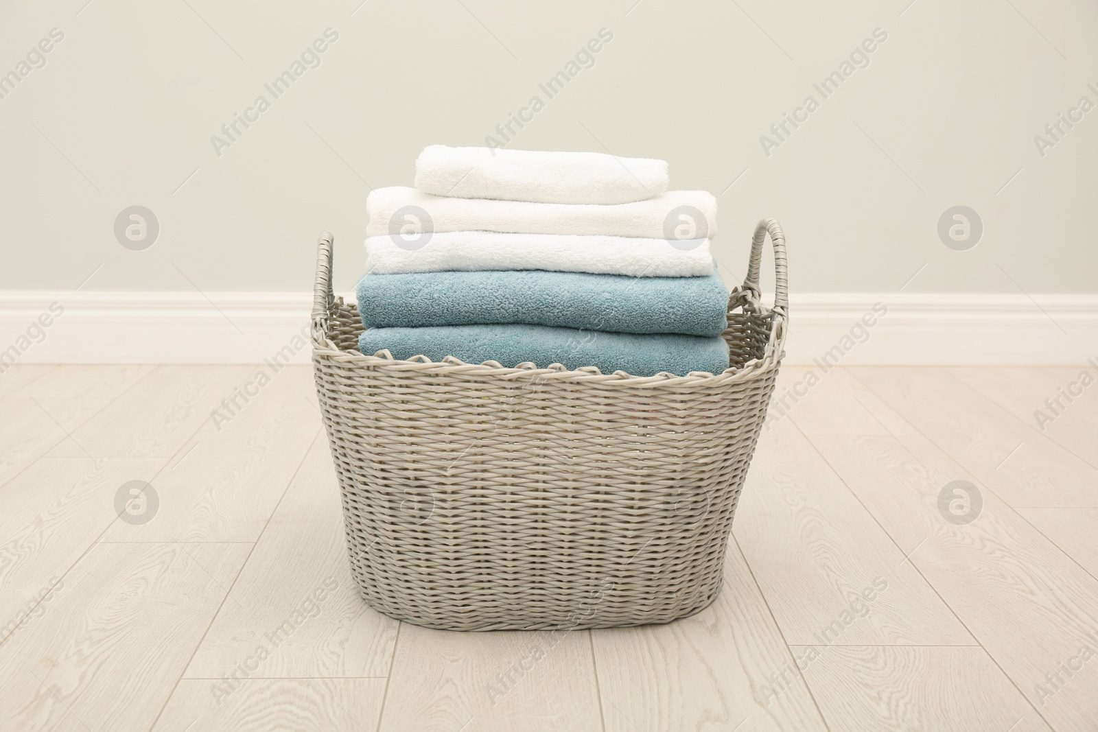 Photo of Wicker basket with folded towels on floor in room