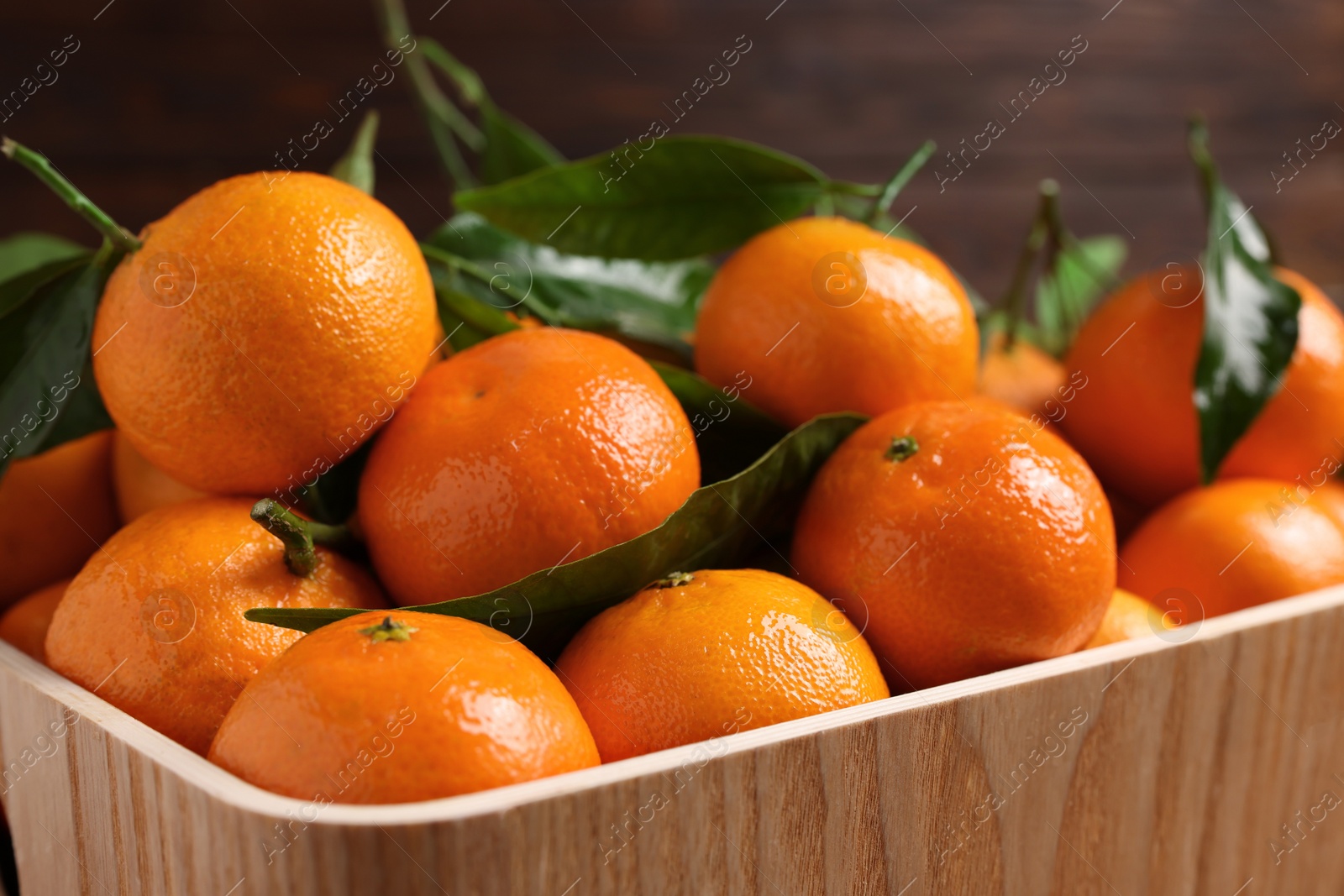Photo of Fresh tangerines with green leaves in wooden crate, closeup
