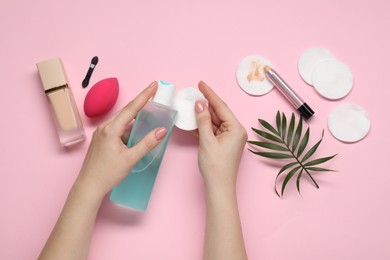 Photo of Woman with makeup remover, cotton pads, foundation, concealer and sponge on pink background, top view