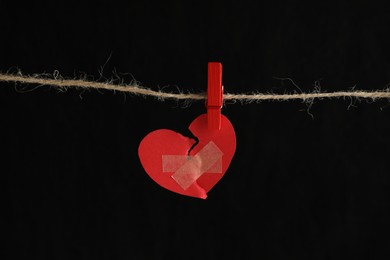 Photo of Broken heart. Torn red paper heart with medical adhesive bandages on black background