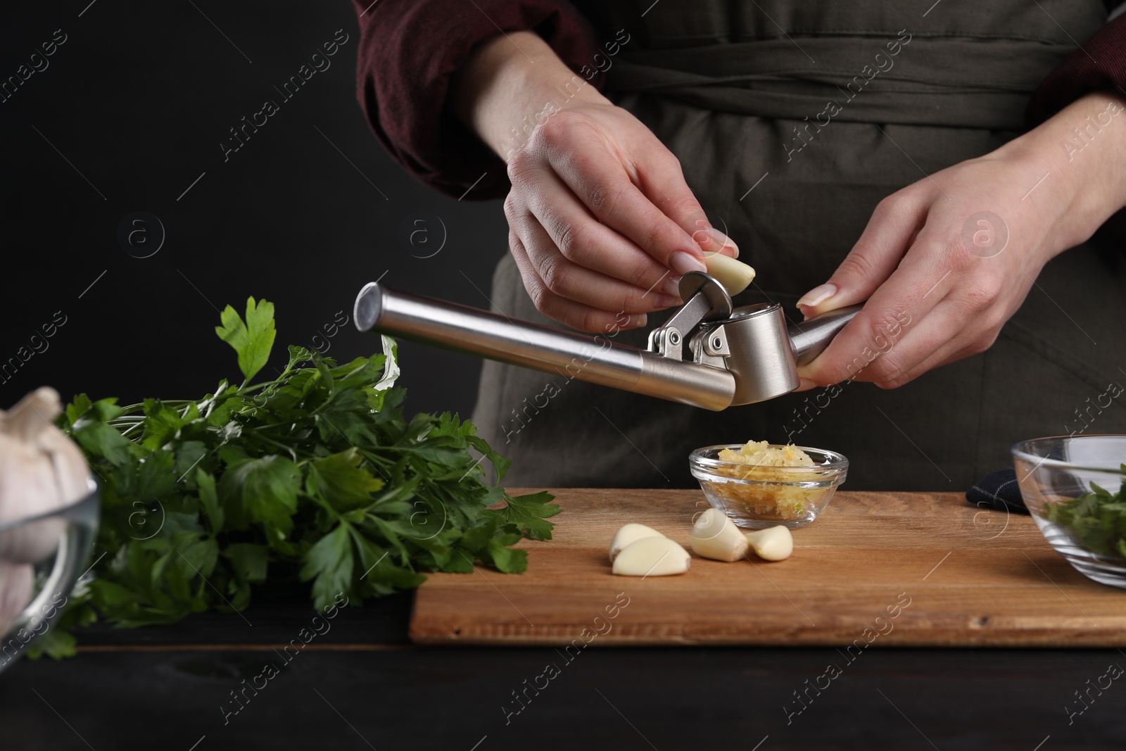 Photo of Woman squeezing garlic with press at black wooden table, closeup