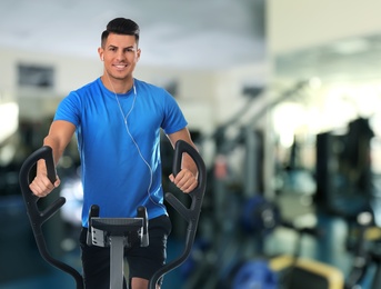 Image of Man using modern elliptical machine in gym, space for text