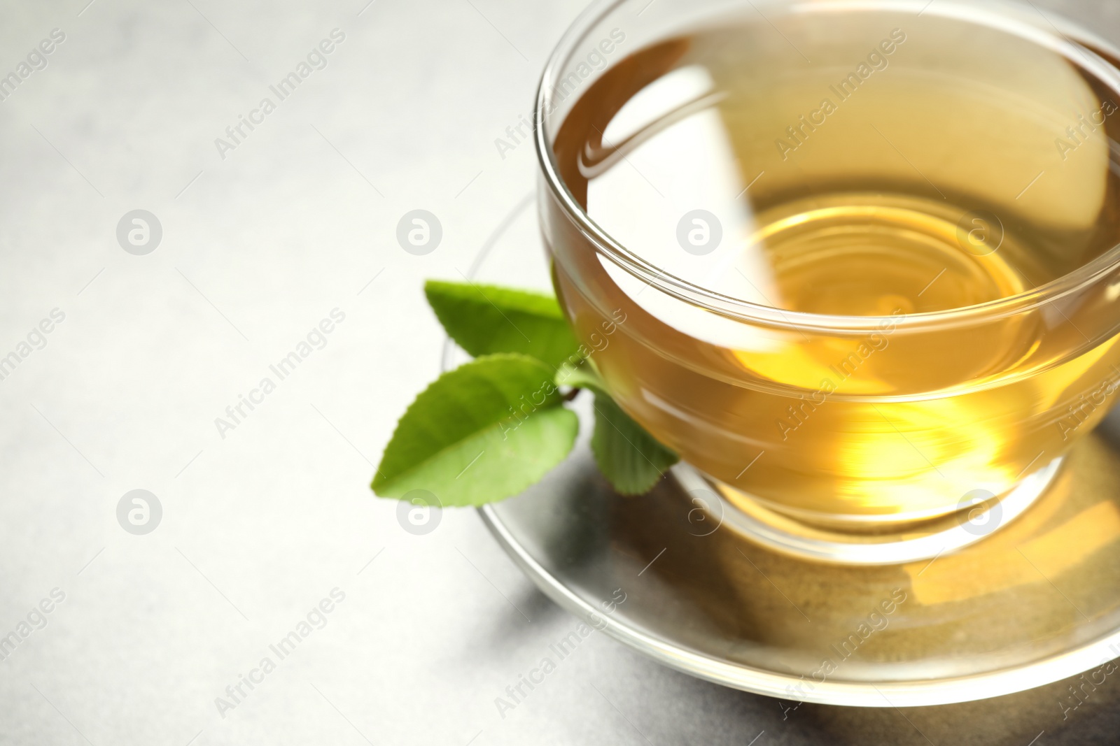 Photo of Cup of green tea and leaves on grey table, closeup. Space for text