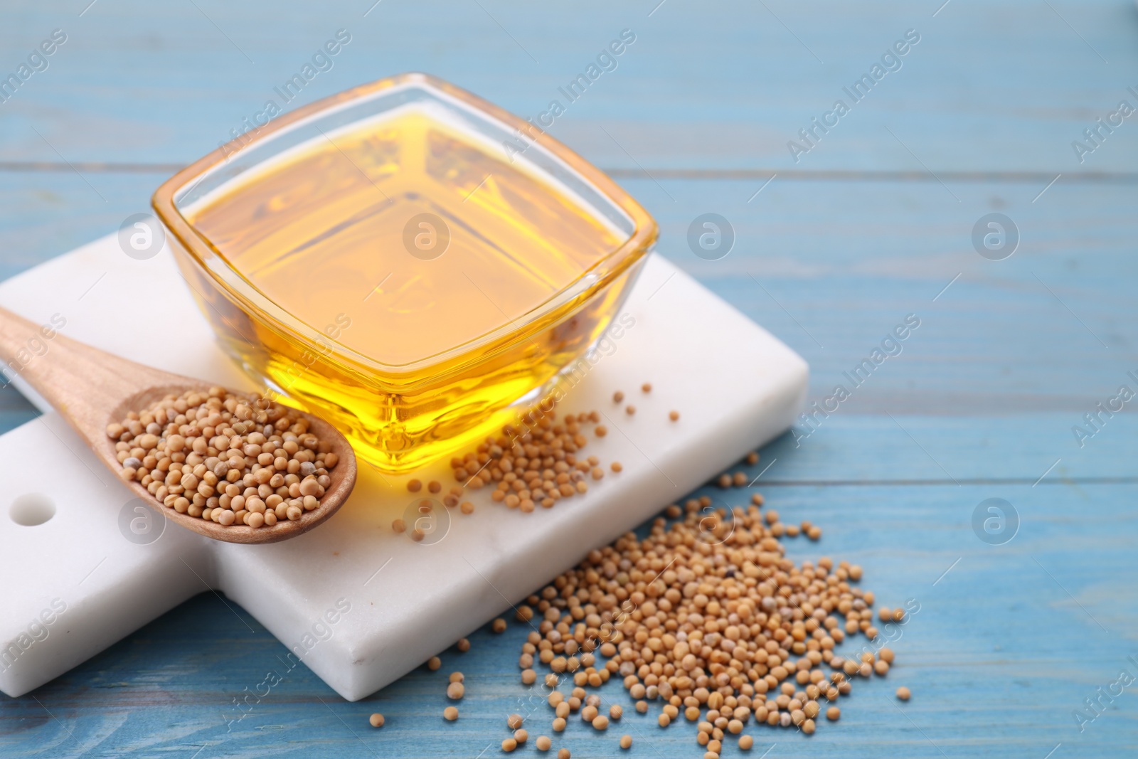 Bowl of natural oil and mustard seeds on light blue wooden table Photo of Bowl of natural oil and mustard seeds on light blue wooden table