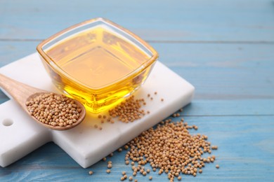 Photo of Bowl of natural oil and mustard seeds on light blue wooden table