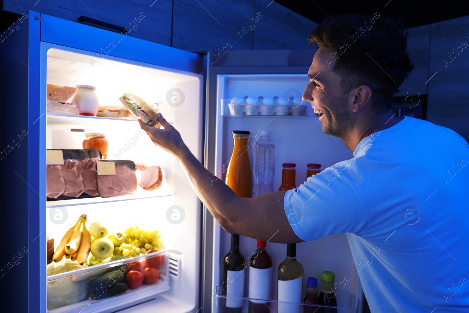 Photo of Man taking sandwich out of refrigerator in kitchen at night