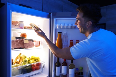 Man taking sandwich out of refrigerator in kitchen at night