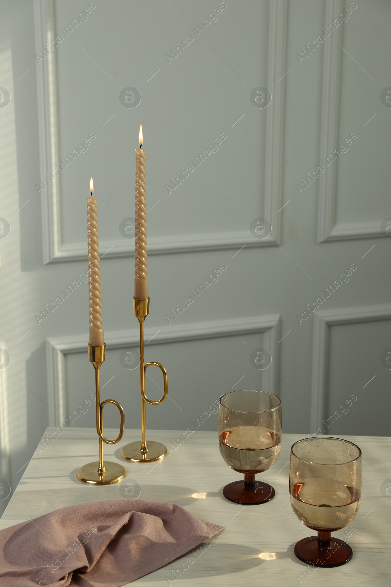 Photo of Glasses of wine near burning candles on white table indoors