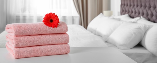 Image of Stack of folded pink towels with red gerbera on bed indoors, space for text. Banner design